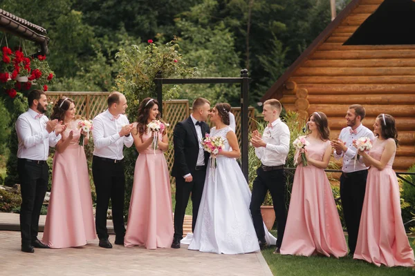 Groom and bride stand with groomsman and bridesmaid outside. Newlyweds kissing and friend clap. Wedding day — Stock Photo, Image