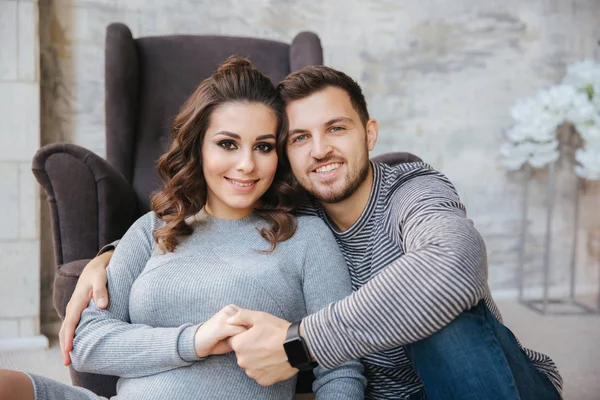 La jeune famille s'assoit près de la chaise et regarde le ventre. Femme enceinte avec son homme bien-aimé. Joyeux couple — Photo