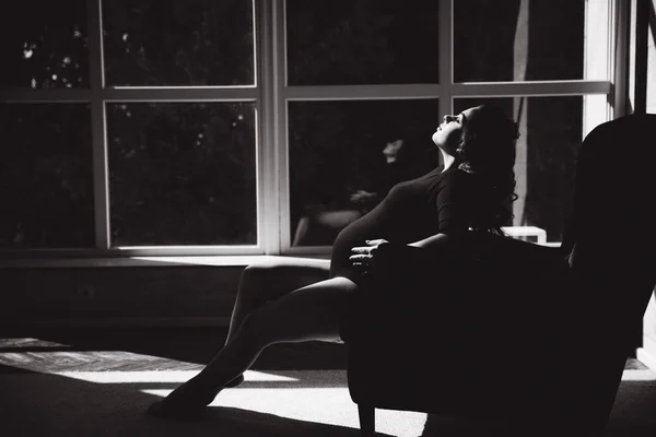 Piękna kobieta w ciąży siedzi na krześle przed dużym oknem. Czarno-białe zdjęcie — Zdjęcie stockowe