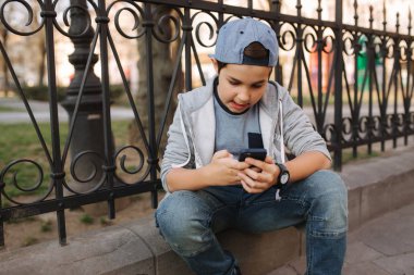 Genç çocuk oyun online oyun dışında smartphone. Şehir merkezinde oturan çocuk. Oğlan oyun oyun süre onun anne gidiş için The dükkan
