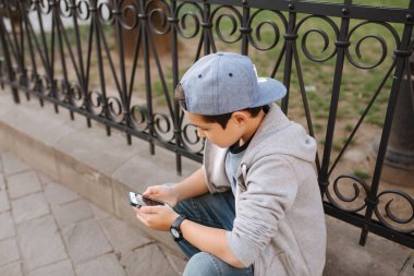 Genç çocuk oyun online oyun dışında smartphone. Şehir merkezinde oturan çocuk. Oğlan oyun oyun süre onun anne gidiş için The dükkan