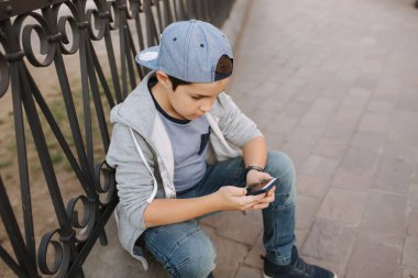 Genç çocuk oyun online oyun dışında smartphone. Şehir merkezinde oturan çocuk. Oğlan oyun oyun süre onun anne gidiş için The dükkan