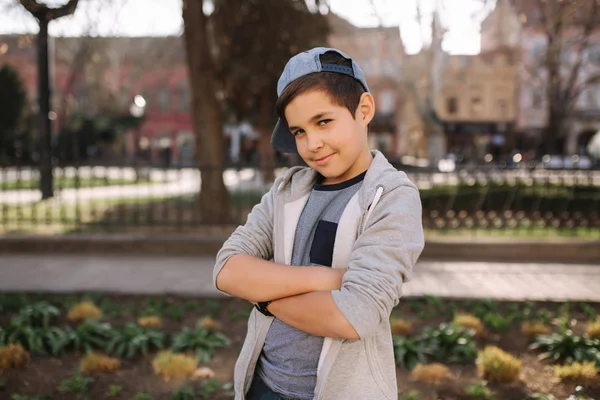 Elegante niño de escuela en gorra azul posando afuera para la foto. Niño caminando en la ciudad en el tiempo sping verano — Foto de Stock