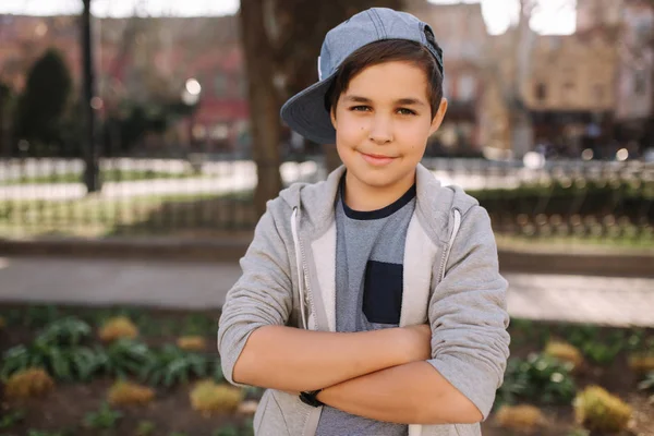 Elegante niño de escuela en gorra azul posando afuera para la foto. Niño caminando en la ciudad en el tiempo sping verano — Foto de Stock