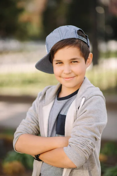Κομψό μικρό σχολείο αγόρι με μπλε καπάκι που ποζάρει έξω για φωτογραφία. Αγόρι με τα πόδια στην πόλη στον καλοκαιρινό καιρό — Φωτογραφία Αρχείου
