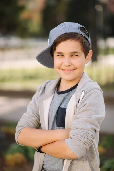 Elegante niño de escuela en gorra azul posando afuera para la foto. Niño caminando en la ciudad en el tiempo sping verano — Foto de Stock