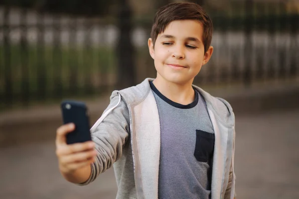 Ung pojke göra en selfie på smartphone i centrum av staden. Söt pojke i blå hatt. Snygg skol pojke — Stockfoto