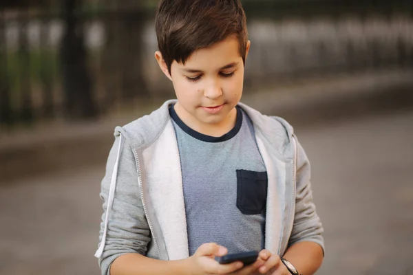 Ung pojke som leker med smaptphone. Schoolboy använder mobil telefon på gatan — Stockfoto