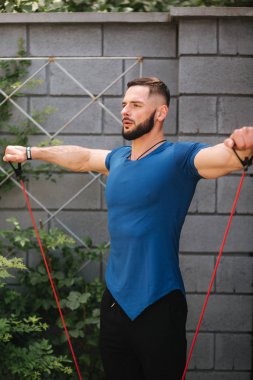 Direnç bandı ile erkek vücut geliştirmeci trenler. Sakallı adam elastik bant ile çalışma