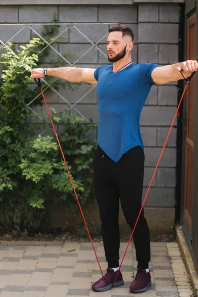 Male bodybuilder trains with resistance band. Bearded man working out with elastic band