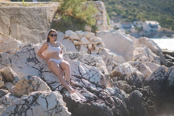 해변에서 바위 위에서 일광욕하는 여자. 수영복을 입은 암컷 과 직업 상 선글라스를 쓴 암컷 — 스톡 사진