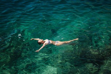 Suda yatan bikinili seksi kadın. Yaz güneşinin tadını çıkaran çekici genç bir kadın. Güzel bir göl. Denizde süzülen bir kadın. Üst görünüm