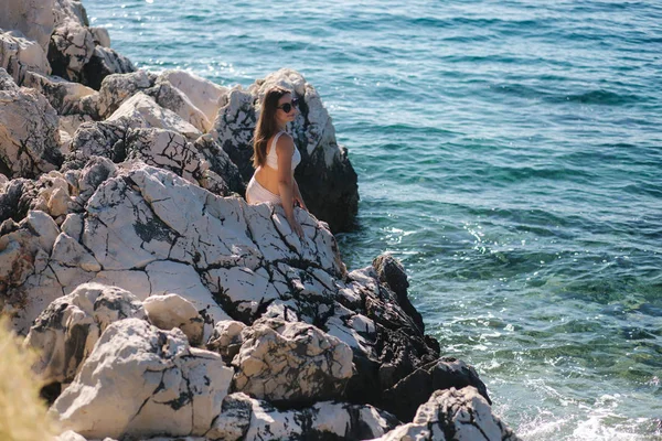 Sexy hembra sentada en la roca en el mar. Atractiva joven mujer en hermoso traje de baño junto al mar. Salpicadura de las olas — Foto de Stock