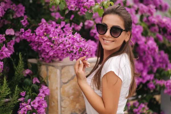 Gyönyörű nő napszemüvegben, gyönyörű virágokkal. Egy boldog, mosolygós fiatal nő portréja — Stock Fotó
