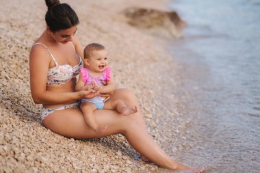 Genç anne deniz sahilde onun bebek kız ile oynamak. Anne ve kızı mayo
