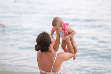 Annenin geri görünümü sahilde onun bebek kız ile oynamak. Denizin arka planı