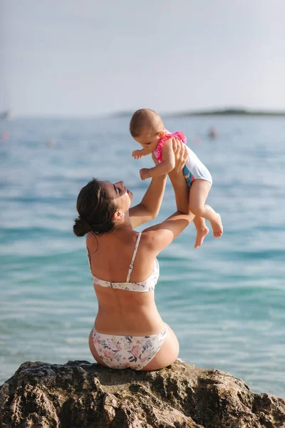 Vedere din spate a mamei fericite cu fetița stă pe piatră în fața mării — Fotografie, imagine de stoc