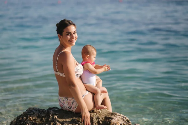 Vedere din spate a mamei fericite cu fetița stă pe piatră în fața mării — Fotografie, imagine de stoc