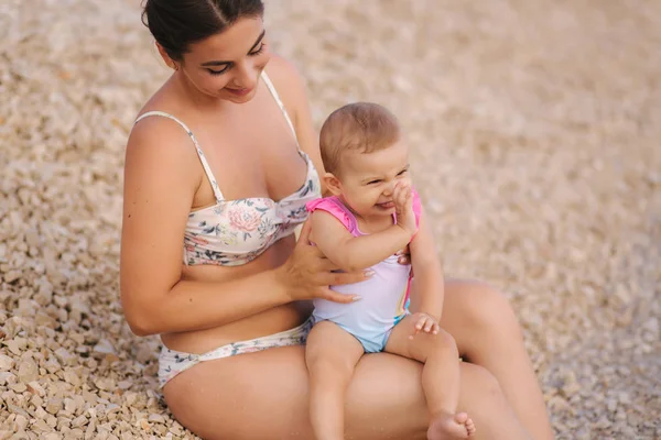 Tânăra mamă se joacă cu fetița ei pe plajă lângă mare. Mama si fiica in costum de baie — Fotografie, imagine de stoc