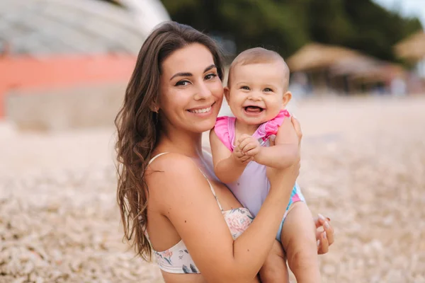 Portrait of cute baby girl with her mother on the beach. Mom with daughter in swimsuit by the sea. Happy baby — Stock Photo, Image