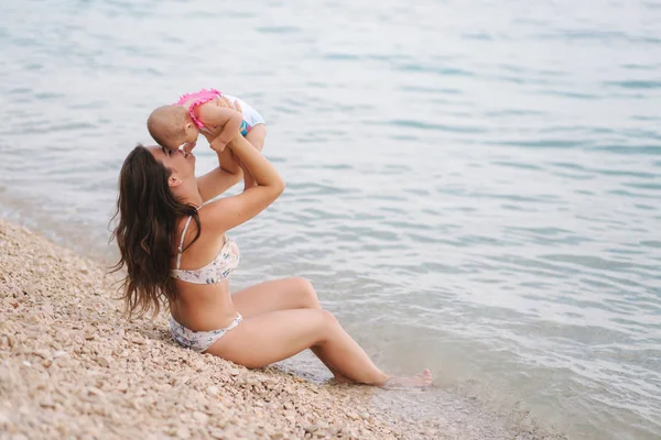 Tânăra mamă se joacă cu fetița ei pe plaja de lângă mare. Apă frumoasă. Familie fericită — Fotografie, imagine de stoc