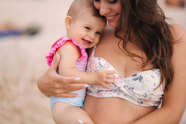 Portretul mamei ține fetița pe mîini pe plaja din mare. Mama şi fiica în costum de baie. Aproape de zâmbetul frumos al bebelușului — Fotografie, imagine de stoc