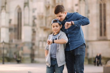 İki kardeş ellerindeki saate bakar. Kardeşim şehirde yürüyor.