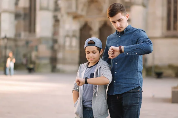 Két testvér nézi az órát a kezükön. Testvér sétál a városban. — Stock Fotó