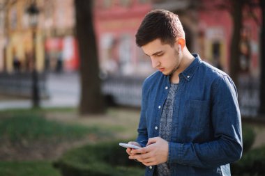 Genç adam sosyal ağda telefon ve kablosuz kulaklıklar ve yazdırma mesajı kullanın