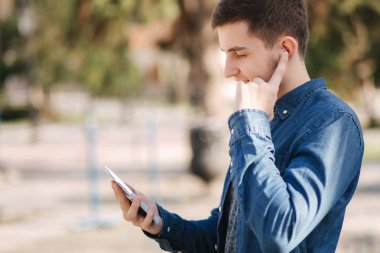 Genç adam sosyal ağda telefon ve kablosuz kulaklıklar ve yazdırma mesajı kullanın
