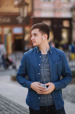Kablosuz kulaklıklar ile mavi kot gömlek genç şık adam. Adam müzik dinliyor