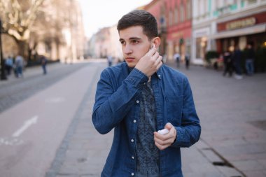 Adam kablosuz kulaklıklarını yerine koydu. Mavi gömlek yakışıklı adam merkezinde stand eğer şehir