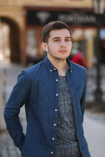 Joven hombre con estilo en camisa vaqueros azules con auriculares inalámbricos. Hombre escuchando una música — Foto de Stock