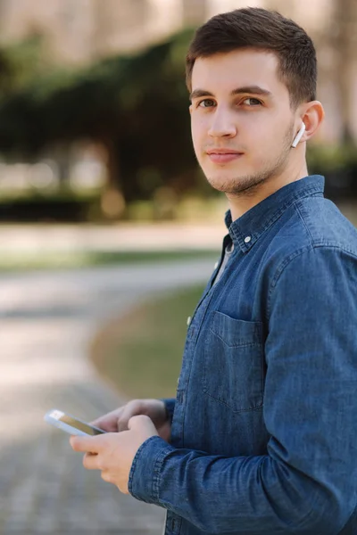 Young stylish man in blue jeans shirt with wireless headphones. Man listening a music — Stock Photo, Image