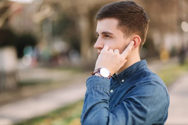 Handsome man put his finger on wireless headphones and speaks. Portrait of man makes conversation by the phone — Stock Photo, Image