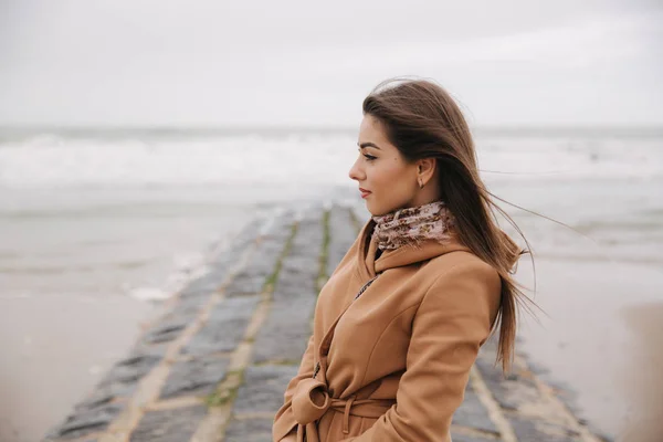 Portré szép nő sétált a tengerparton, közel az Északi-tengeren. Elegáns hölgy barna kabátot divat töltsük fel állni a tenger előtt — Stock Fotó