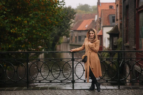 Mulher elegante em casaco castanho em pé na ponte em Bealgium, Brugge. Feminino colocar em um capuz — Fotografia de Stock