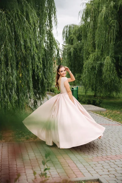 Fashionable girl spin around in park. Evening dress