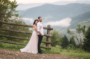 Sevimli gelin dağlarda onu yakışıklı damat sarılmak. Güzel düğün çift yürüyüş. Yeşil gackground
