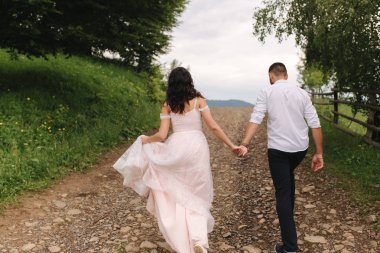 Sevimli gelin dağlarda onu yakışıklı damat sarılmak. Güzel düğün çift yürüyüş. Yeşil gackground