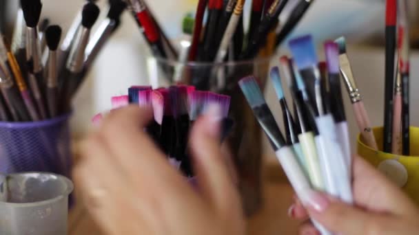 Donna scegliere pennello per la pittura. Concetto artistico. Ci sono un sacco di pennelli nello studio di disegno. Primo piano delle mani con pennello — Video Stock