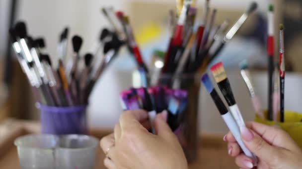 Donna scegliere pennello per la pittura. Concetto artistico. Ci sono un sacco di pennelli nello studio di disegno. Primo piano delle mani con pennello — Video Stock