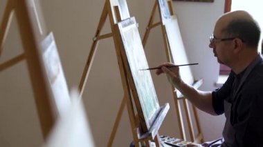 Gözlük yetişkin erkek sanatçı fırça ve yağlı boya kullanarak bir resim boyama. Sanat konsepti. Yaratıcı mutlu ressam renkli bir resim çizer. Çizim stüdyosu