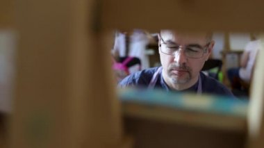 Gözlük yetişkin erkek sanatçı fırça ve yağlı boya kullanarak bir resim boyama. Sanat konsepti. Yaratıcı mutlu ressam renkli bir resim çizer. Çizim stüdyosu