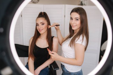 Fotoğraf makyaj sanatçısının yüzük lambası çekici genç kız için bir makyaj yapıyor olsa. Beyaz katlanır ekranın arka planı