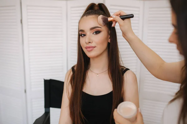 Maestro trucco femminile utilizzare una spazzola a polvere. Bella modella in studio di bellezza. Trucco professionale artista finitura malup moda. Sfondo dello schermo pieghevole bianco — Foto Stock