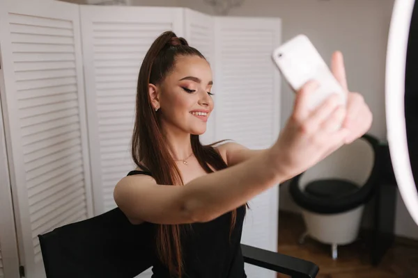 Joven modelo atractiva hacer una selfie después del maquillaje en el estudio de belleza. Ella usa un anillo lapm para la foto. Fondo de pantalla plegable blanca — Foto de Stock