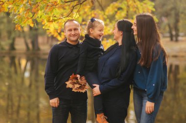 Annem ve babam iki kızı ile orada park eğlenmek. Genç kızı toplamak yaprakları ve gülümseme. Mutlu aile ormanda yürüyüş