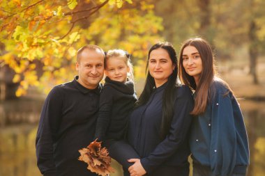 Annem ve babam iki kızı ile orada park eğlenmek. Genç kızı toplamak yaprakları ve gülümseme. Mutlu aile ormanda yürüyüş