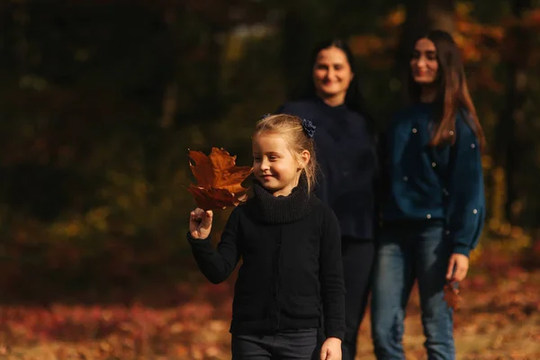 小女孩在森林里收集树叶。背景的妈妈, 爸爸和妹妹。年轻的家庭在秋天公园 — 图库照片